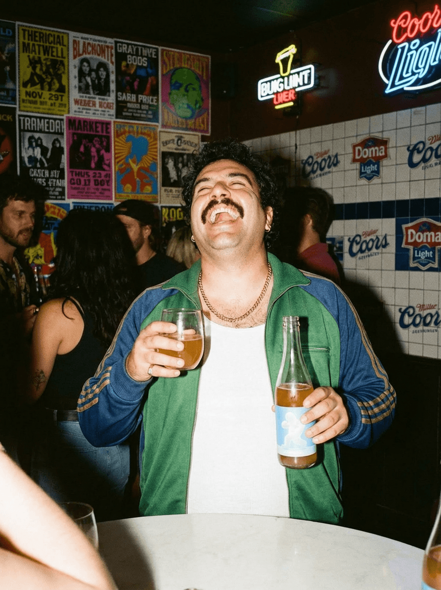 Laughing with a Liquid Dreams bottle in a dive bar