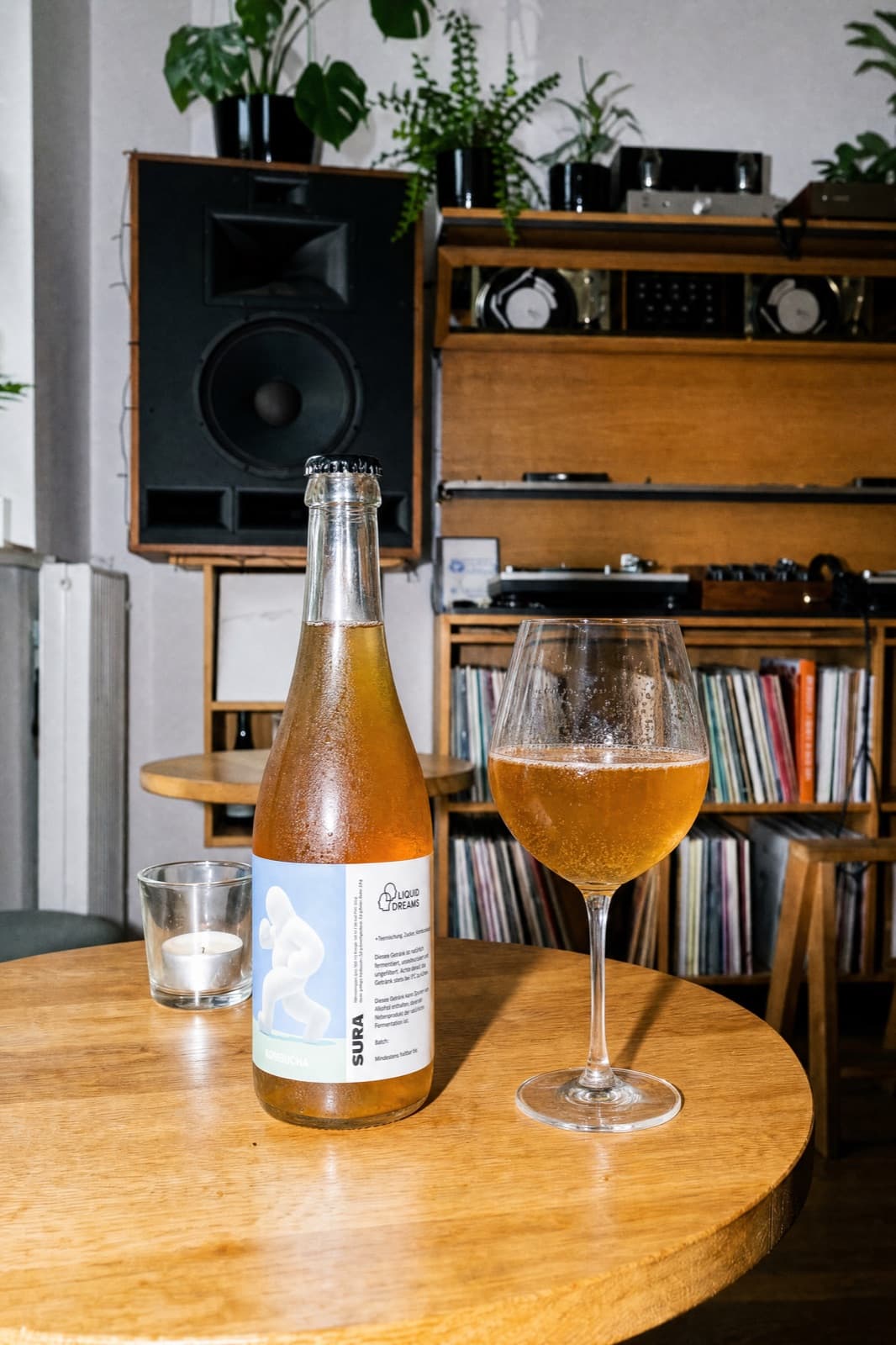 A glass of SURA poured beside the bottle on a wooden table, a Berlin listening-room behind